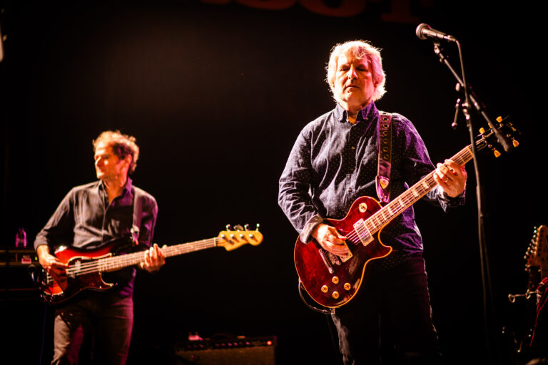 Twee muzikanten op het podium, één met een elektrische gitaar en de ander met een basgitaar.