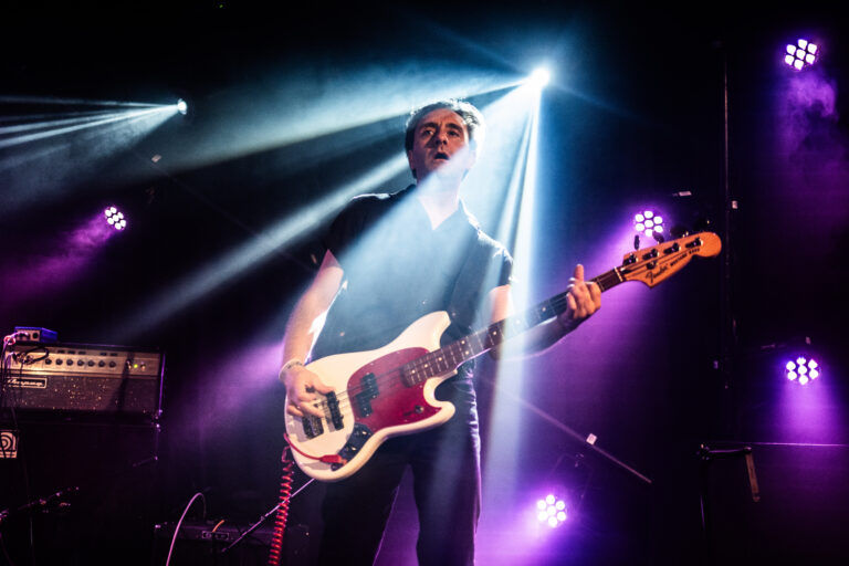 Een muzikant speelt op een elektrische basgitaar onder fel licht tijdens een live optreden.