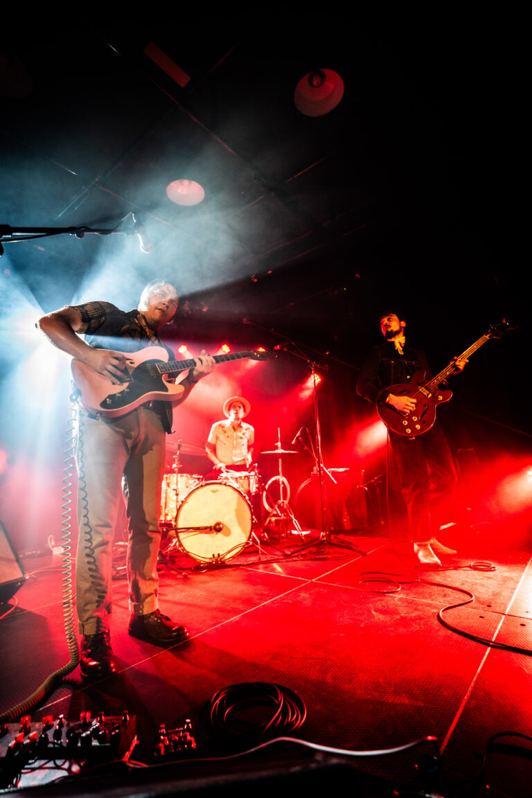 Een live band speelt op een podium met dramatische verlichtingen in rode en blauwe tinten.