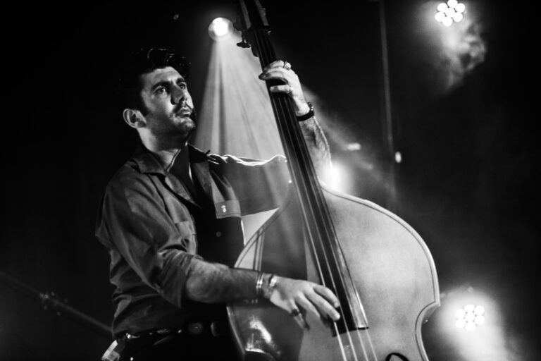 Een muzikant speelt enthousiast op een contrabas onder het podiumlicht.
