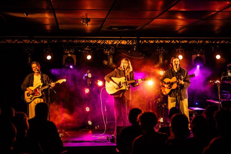 Een muziekgroep die optreedt op een podium met kleurrijke belichting en een publiek voor hen.