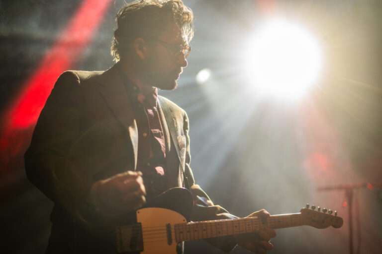 Een muzikant speelt gitaar op het podium, verlicht door krachtige spotlights.