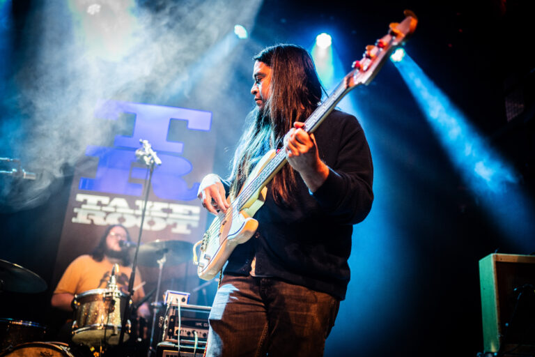 Een muzikant speelt basgitaar op een podium met blauwe verlichting.