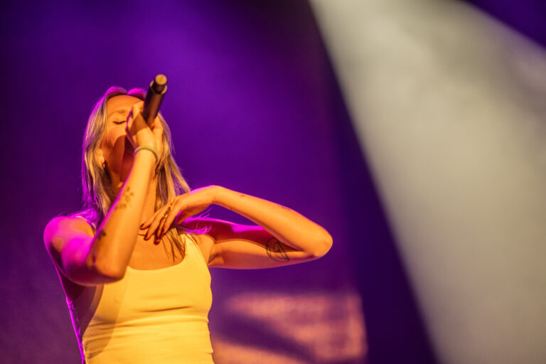 Een vrouw met een microfoon zingt op een podium met kleurrijke verlichting.