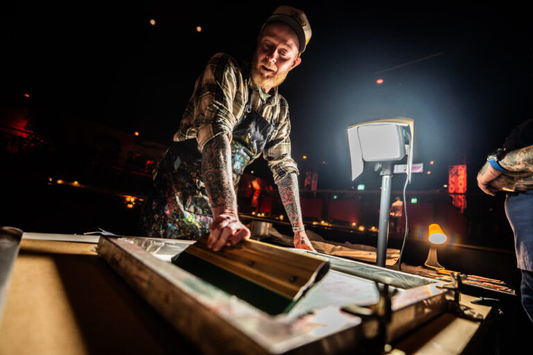 Een artiest die bezig is met zeefdrukken, met een drukpers en een werklicht in een sfeervolle omgeving.