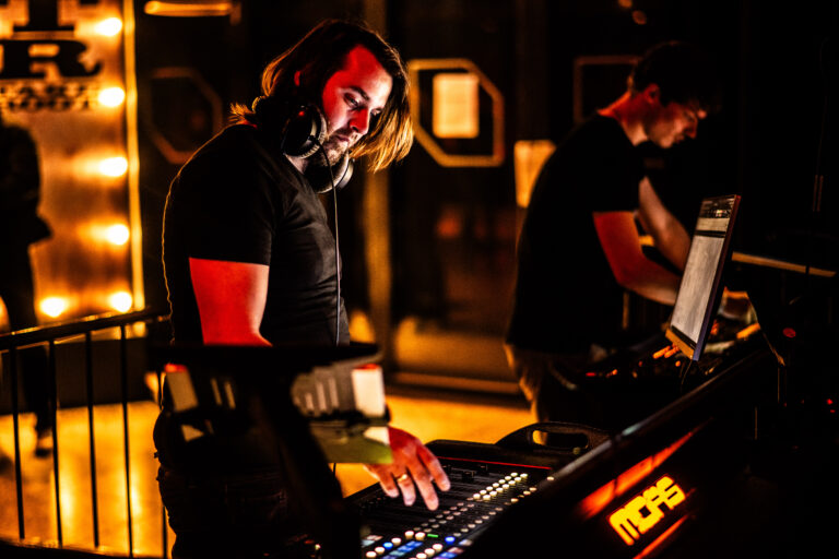 Een DJ draait muziek achter een mengpaneel in een donkere club met sfeerverlichting.