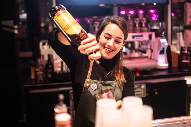 Een barmixer met een glimlach schenkt een drankje in een glas aan de bar.