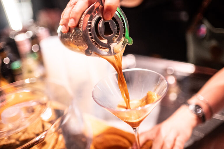 Een hand giet een drankje vanuit een zeef in een cocktailglas.