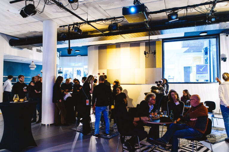 Een groep mensen staat in een zaal tijdens een presentatie.