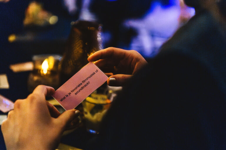 A person holding a pink card at a dimly lit social gathering.