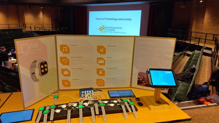 Op tafel staan meerdere programmeerbare hardwarekits met aansluitende kabels, terwijl op de achtergrond een presentatie op een scherm wordt getoond.