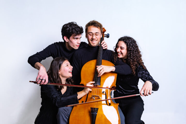 Een groep van vier jonge muzikanten poseert samen rond een cello, met blije gezichten en zwarte kleding.