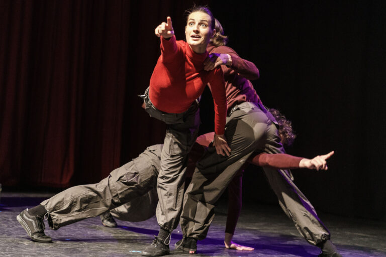 Een groep dansers voert een dynamische choreografie uit op een podium met een zwarte achtergrond.