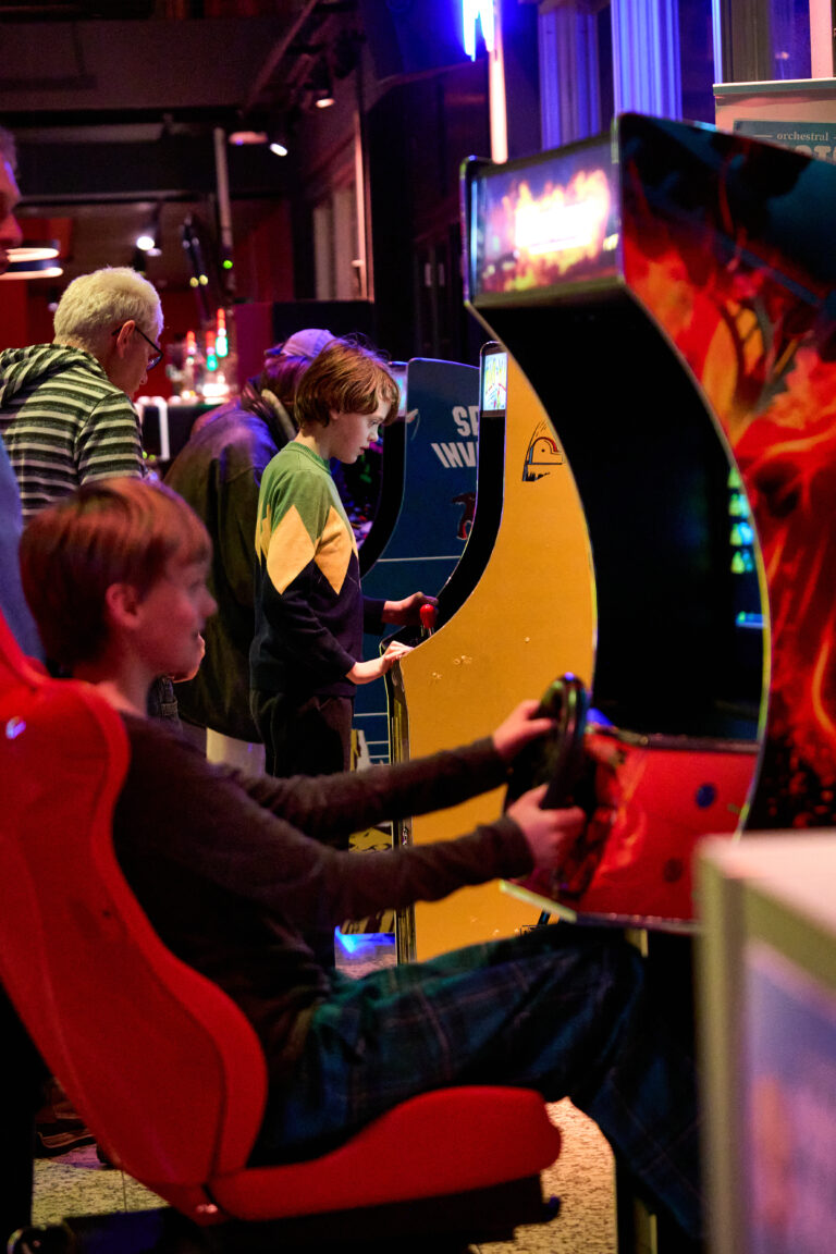 Meerdere mensen spelen aan arcadeautomaten in een kleurrijke arcadehal.