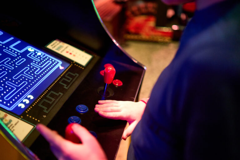 Close-up van een persoon die een arcadegame bedient, met een hand op de joystick en knoppen.