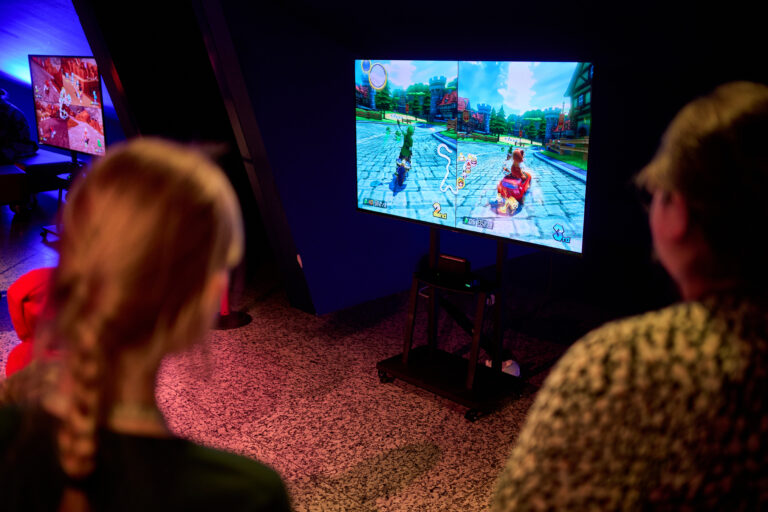 Twee mensen kijken naar een televisiescherm waarop een videospel wordt gespeeld.