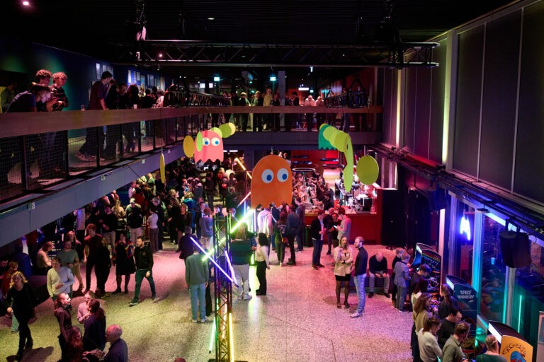 Een levendig evenement met een drukke menigte in een zaal, versierd met kleurrijke elementen en verlichting.