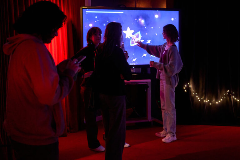 Een groep silhouetten staat in een donkere zaal en kijkt naar een grote, heldere projectie op een scherm.