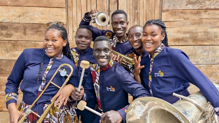 Een groep muzikanten in blauwe uniformen poseert met verschillende blaas- en slagwerkinstrumenten.