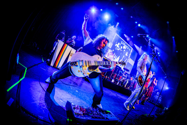 Een gitarist speelt gitaar op een verlicht podium tijdens een rockconcert.