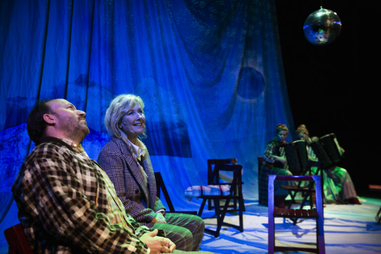 Een groep mensen zit op stoelen op een blauw verlicht podium.