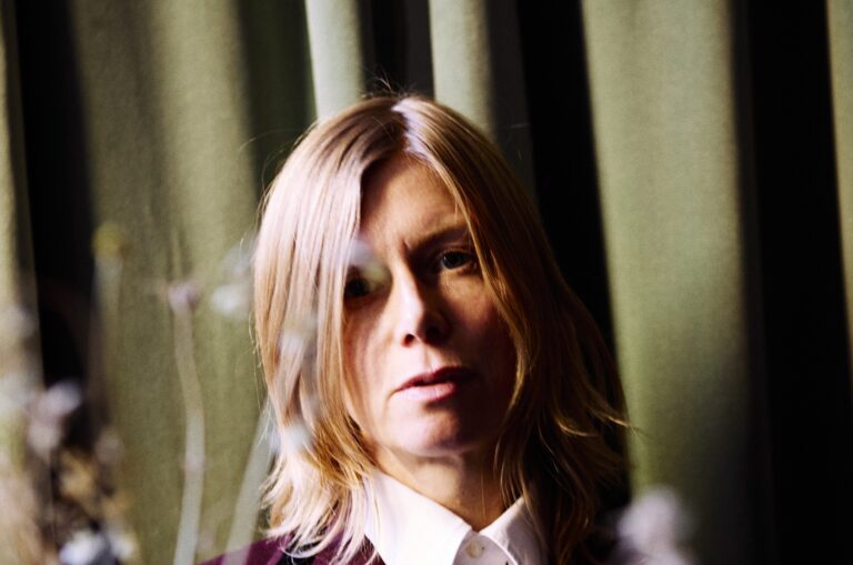 Portret van een vrouw met lang blond haar die in de camera kijkt.