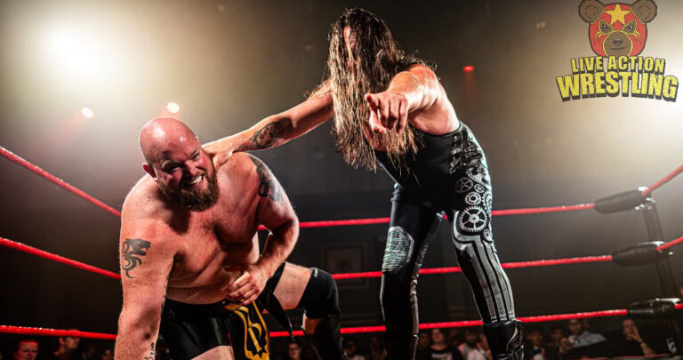 Twee worstelaars in een ring tijdens een gevecht; de shirtloze man buigt voorover terwijl de ander met lange haren een beweging uitvoert.