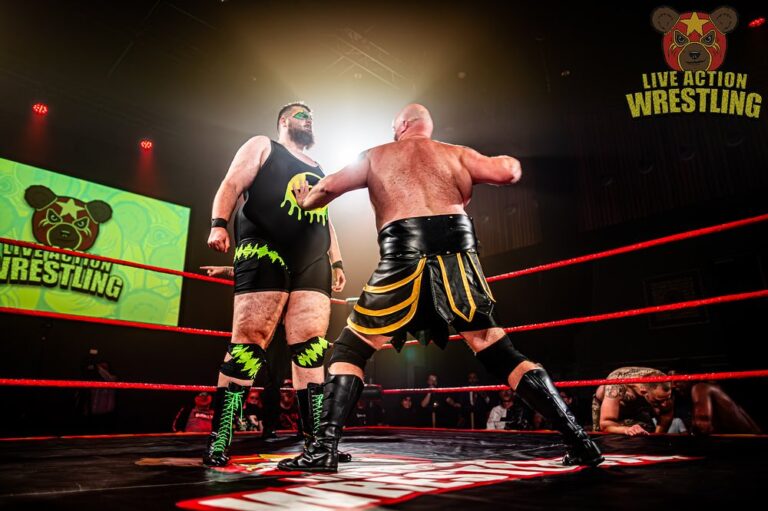 Twee worstelaars strijden in een ring tijdens een wedstrijd, terwijl ze elkaar vasthouden onder fel podiumlicht.