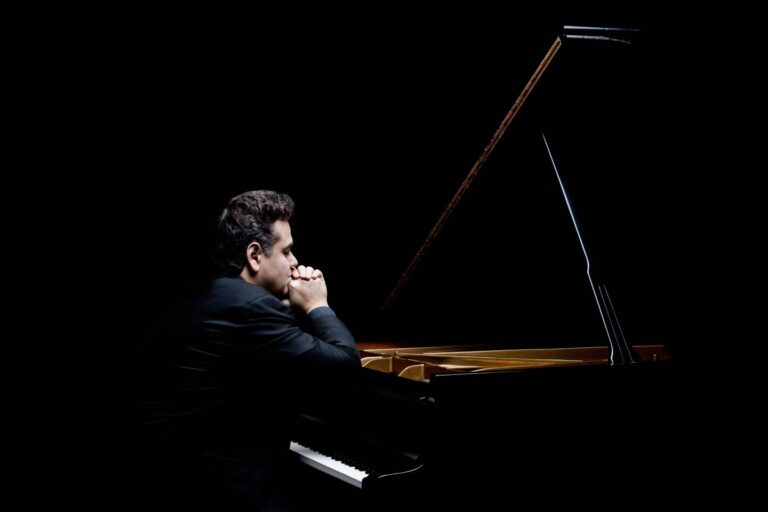 Een pianist zit in een donkere ruimte achter een vleugelpiano.