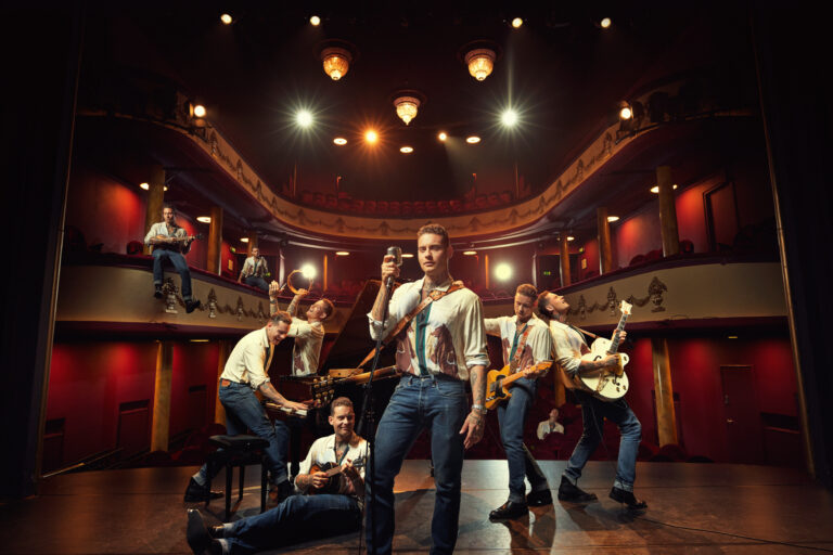 Een groep muzikanten poseert op een podium in een sfeervol theater met warme verlichting.