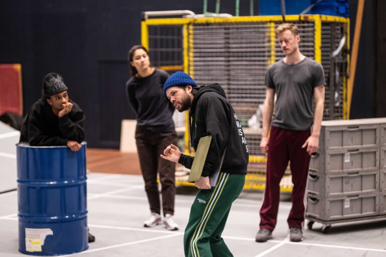 Een groep mensen in sportkleding staat in een binnenruimte, terwijl een man in het midden voorover buigt.