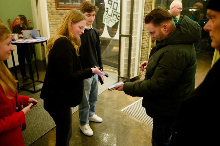 Vier mensen staan in een winkel en bekijken samen een smartphone.