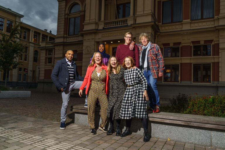 Een groep mensen poseert samen op de trappen voor een statig bakstenen gebouw.