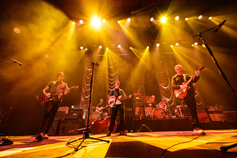 Een muziekband speelt live op een podium onder fel gele lichten.