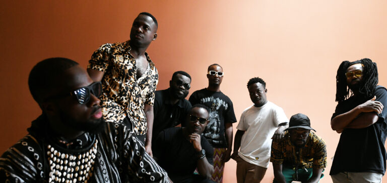 Vier mannen staan samen voor een oranje muur.