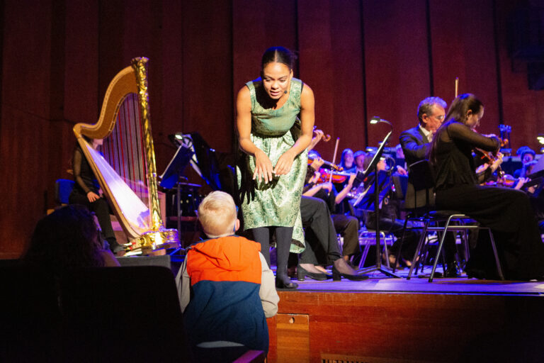 Een vrouw in een groene outfit staat centraal op een podium, met een live-band op de achtergrond.