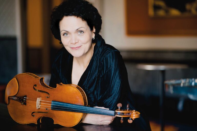 Een glimlachende vrouw houdt een viool vast.