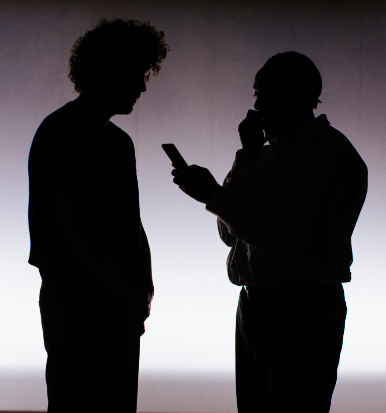 Twee silhouetten van mensen in gesprek tegen een lichte achtergrond, waarbij één persoon een handgebaar maakt.