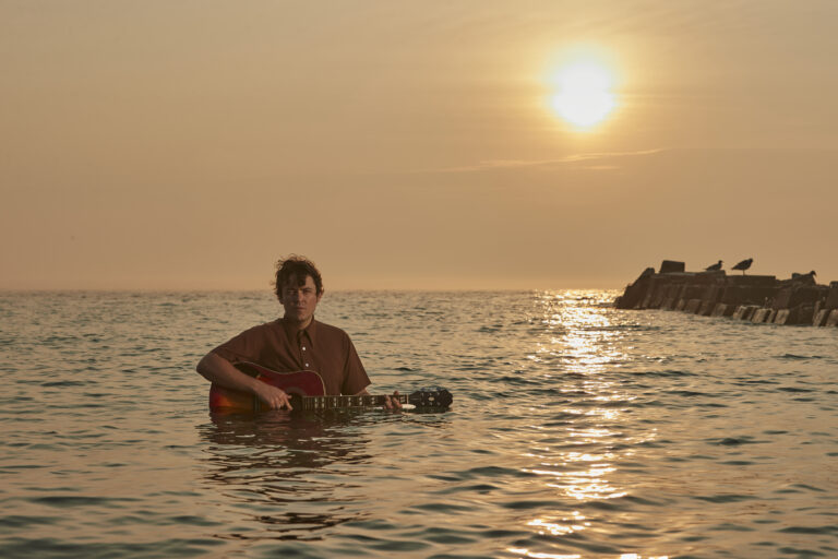 Een persoon speelt gitaar in het water tijdens een zonsondergang.