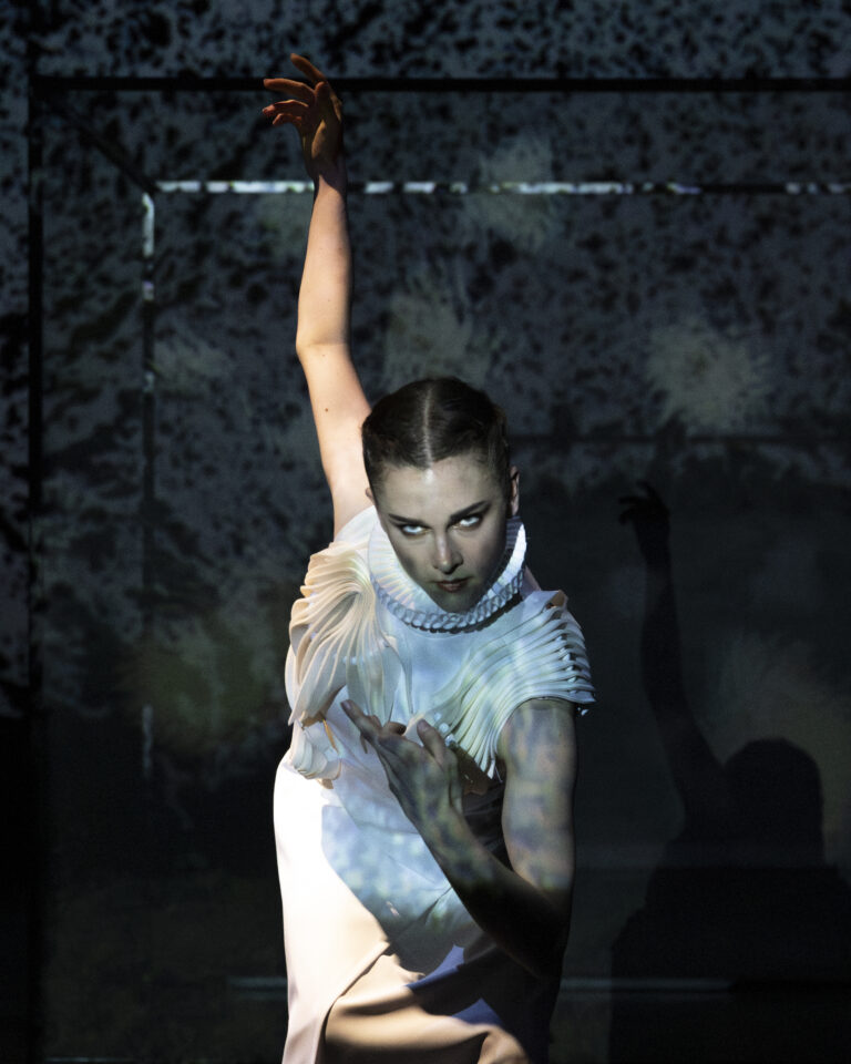 Een performer in een opvallende outfit poseert dynamisch tegen een abstracte achtergrond.