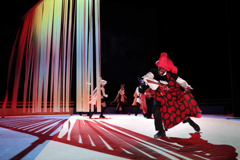 Een levendige theaterperformance met dansers in kleurrijke kostuums op een verlicht podium.