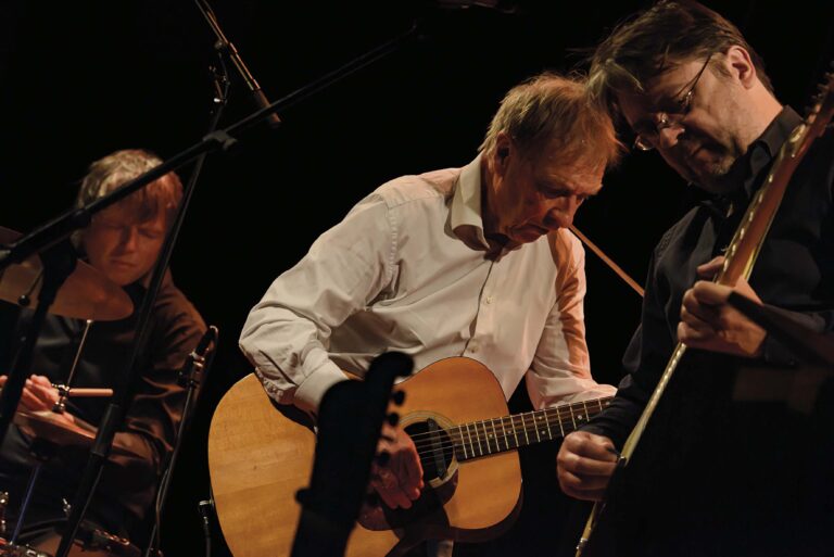 Een man speelt een akoestische gitaar op een podium tijdens een optreden.