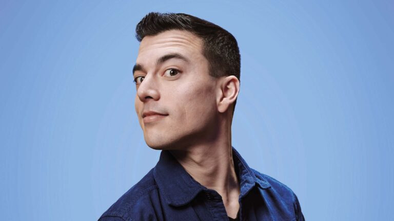 Portret van een man met kort donker haar tegen een lichtblauwe achtergrond.