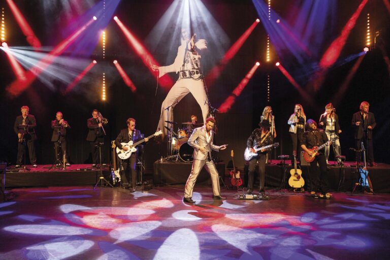 Zangeres op een fel verlicht podium tijdens een live optreden, met muzikanten op de achtergrond.