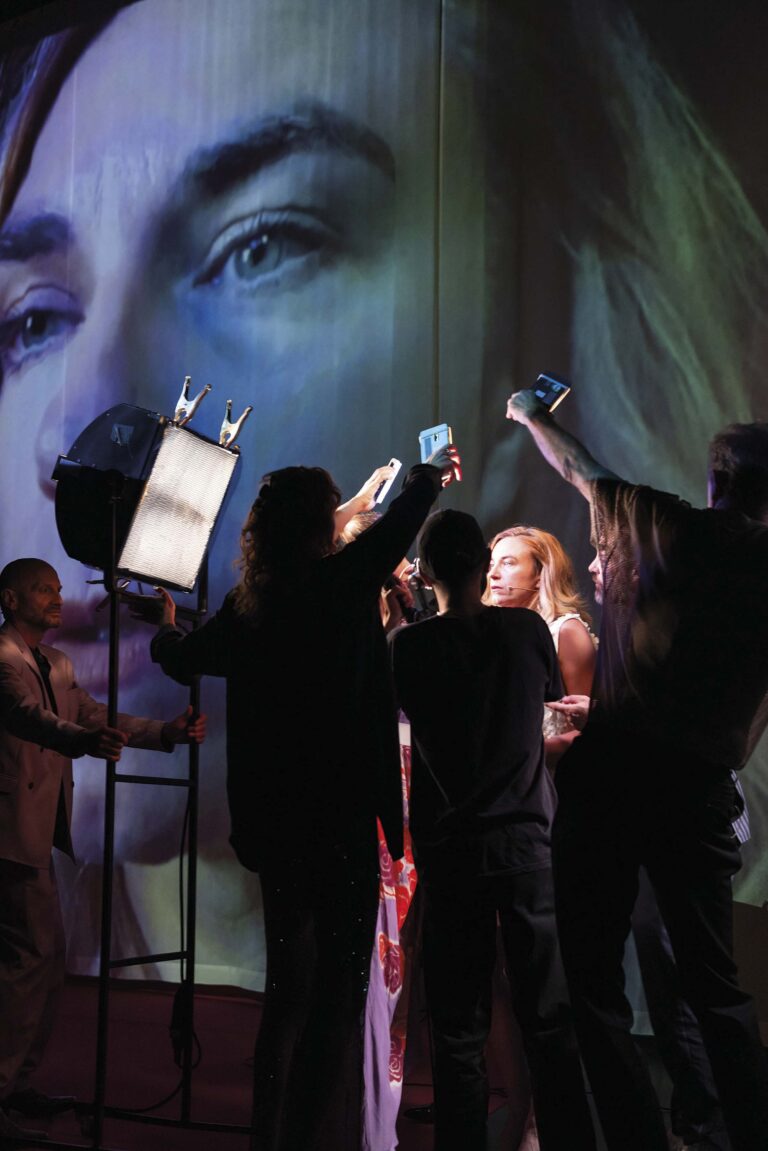 Een groep mensen op een podium voor een achtergrond met een grote afbeelding van een gezicht.