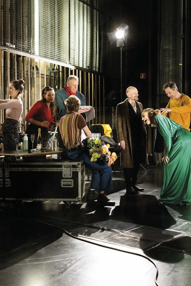 Meerdere muzikanten en zangers op een podium tijdens een liveoptreden, met een vrouw in een felgroene jurk.