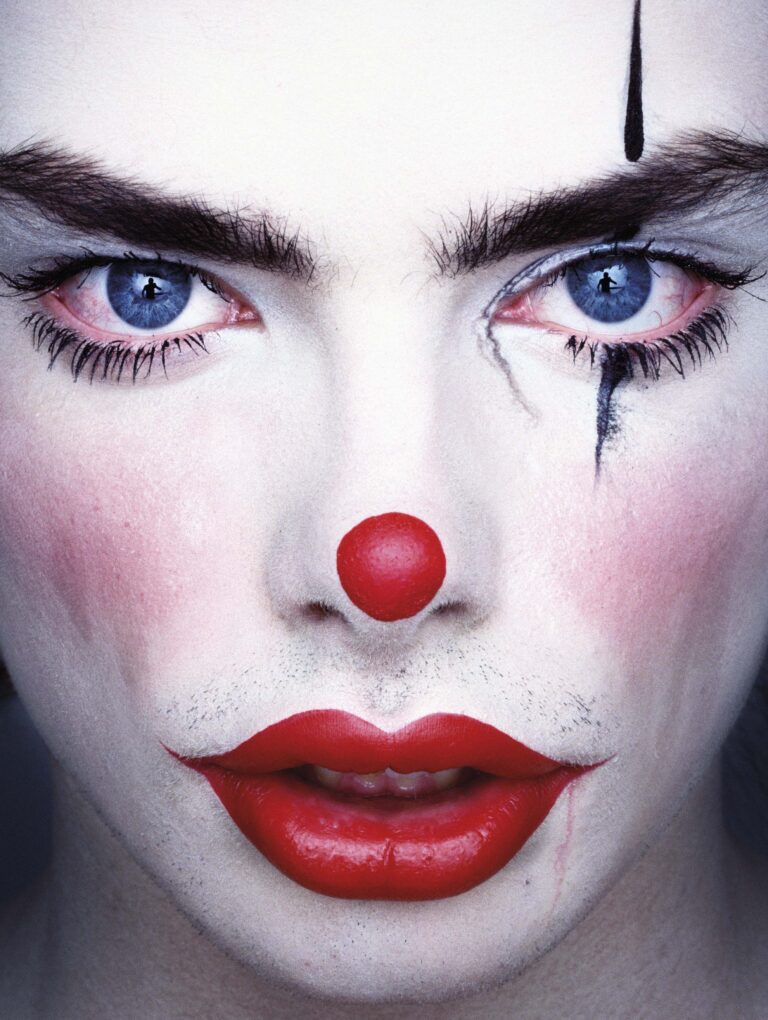 Close-up van een clown met witte gezichtsmake-up en een opvallende rode neus.