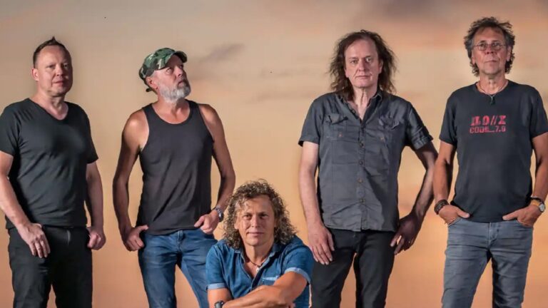 Drie muzikanten poseerden tegen een achtergrond van een kleurrijke lucht.