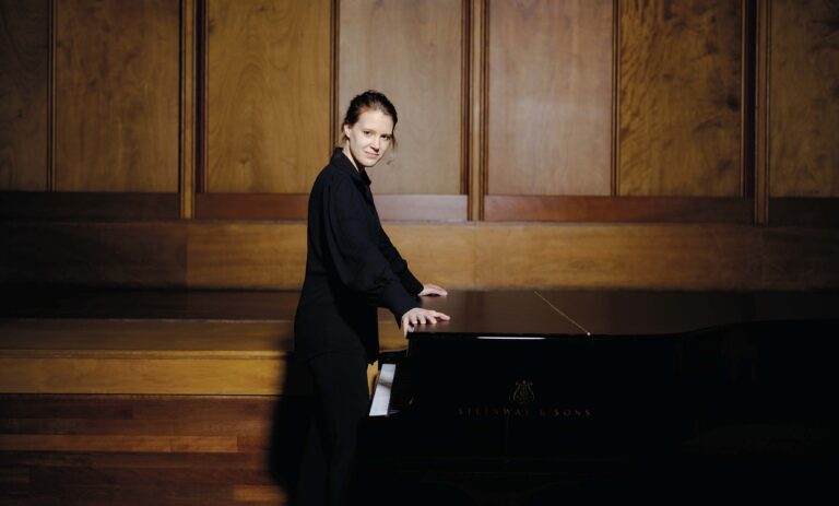 Een man in een donker pak speelt een piano op een houten podium.