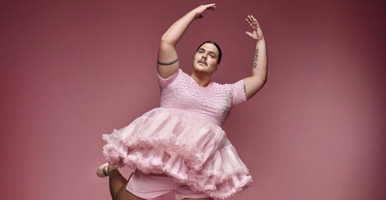 Een persoon in een roze, ruchesachtige jurk danst tegen een roze achtergrond.